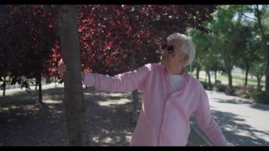 Madrid 'den gelen pembe tişörtlü enerjik son sınıf öğrencisi, huzurlu bir şehir parkında güneşli bir yürüyüş sırasında bir ağaçla eğlenceli bir şekilde etkileşime giriyor..