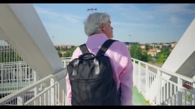 Beyaz saçlı ve sırt çantalı kıdemli İspanyol adam, berrak mavi gökyüzünün altındaki Madrid 'in kenar mahallelerinin manzarasına hayran olmak için bir köprüde sabah yürüyüşünün tadını çıkarıyor..