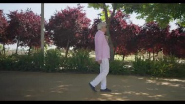 Madrid 'den gelen pembe tişörtlü ve beyaz pantolonlu yaşlı bir adam, bir matematik dersine giderken kolunun altında bir klasör taşıyarak güneşli bir parkta düşünceli bir şekilde yürüyor..