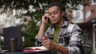 Kafe masasında çalışırken bir telefon görüşmesine odaklanmış genç bir adam.