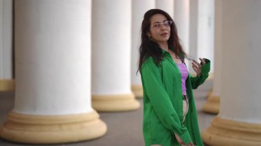 Canlı yeşil gömlekli şık bir birey çarpıcı mimari sütunlarla zarif ve emin bir şekilde poz verir.