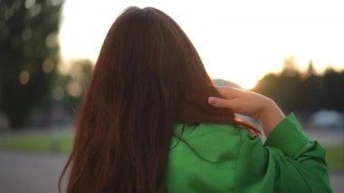 Yeşil gömlekli neşeli bir kadın neşe içinde büyüleyici bir günbatımına hayran, kendine güven ve cazibe saçıyor.