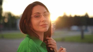 Yeşil tişörtlü bir kadının büyüleyici portresi, günbatımından zevk alıyor ve tarzını sergiliyor..