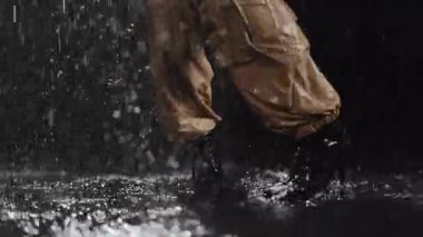 Yağmurdaki dinamik hareketin büyüleyici bir görüntüsü, cesur moda ve canlı su yansımaları sergiliyor.