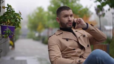 İyi giyimli bir adam sakin bir şehir parkında otururken cep telefonuyla canlı bir sohbete girişir.