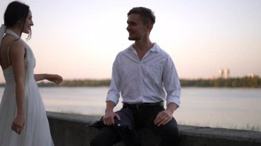 Beyaz elbiseli gelin beyaz gömlekli damadını öpmek için eğildi. Birbirlerini suya yakın tutarlar, şefkat ve sevgi dolu samimi bir yavaş çekim anını paylaşırlar..