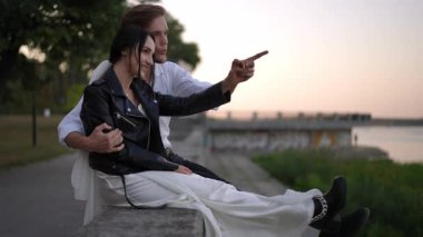 Alacakaranlıkta nehir kıyısında, çift neşeyle güler. Kadın tamamen giyinik ve nallı, beyaz bir elbise, deri ceket ve zincirli botlar giyiyor, adam onu yavaş çekimde tutuyor..