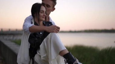 Alacakaranlıkta nehir kenarında, ona sarılıyor ve yanağından öpüyor. Deri bir ceketin altında tamamen giyinik ve nallı beyaz bir elbise giyiyor. Ağır çekimde yakalanan siyah çizmeler. Modern düğün gecelerinden bir neşe molası..