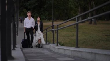 Şık genç çift parkta birlikte yürüyor. Adam bavulu çekiyor ve kadın deri ceketli, sakin bir akşamın tadını yavaş çekimde çıkarıyor.