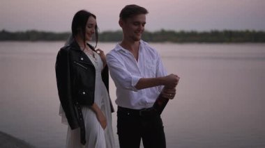 Gelin şaşkınlıkla gülerken damat nehir kenarında bir şişe şampanya açar. Çift, neşe ve kutlamalarla dolu ağır çekim sahnesinin tadını çıkarıyor..