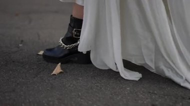 Gelin, siyah çizme ve zincir detaylarıyla beyaz gelinlik içinde yürüyor. Zarafetle modern tarzı birleştiriyor..