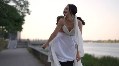 Beyaz elbiseli mutlu gelin, damat tarafından nehir kenarında kaldırılırken kollarını açar. Düğün gününün kaygısız sevgisini ve neşesini gösterir..