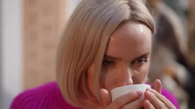 Rahat pembe bir kazak giymiş bir kadın sıcak ve rahatlatıcı bir içecekten zevk alır. Huzurlu bir anı mükemmel bir şekilde taşır.