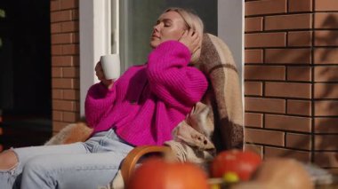 Bir kadın, canlı sonbahar elementleriyle çevrili sıcak ve rahat bir ortamda lezzetli kahvesinin tadını çıkarıyor.