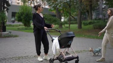 İki kadın, huzurlu bir park ortamında bebek arabasıyla ilgilenirken şefkatli ve samimi bir anı paylaşıyor.