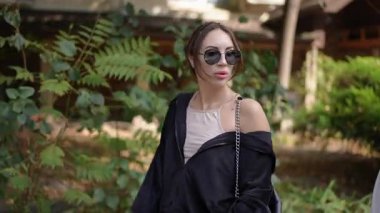 İki şık kadın, şık kıyafetlerini giyerken yemyeşil alanda keyifli ve rahat bir şekilde yürürler.