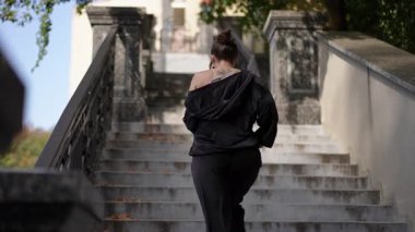 Şık siyah elbiseli bir kadın zarif bir şekilde merdiven çıkıyor, şehir keşfi ve akıcılık sergiliyor.