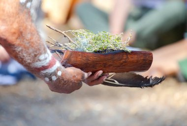 Avustralya 'da bir yerel halk etkinliğinde dumanla yapılan ayin olan Avustralya bitki dallarıyla dolu ahşap tabağı insan eliyle tutuyor.
