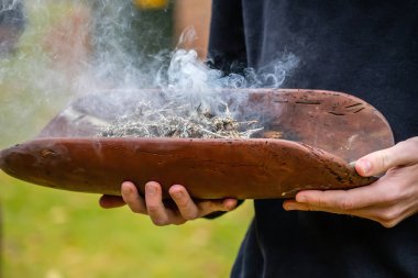 Human hands with green branches and ritual dish, smock rite at indigenous reconciliation event in Australia, symbol of joining to indigenous culture clipart