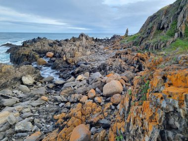 Güney Avustralya 'da okyanus kıyıları, kayalar, alışılmadık kırmızı taşlar. Bulutlar ve çizgiler. Deniz Burnu. 