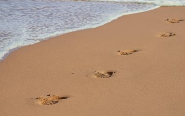 Deniz kıyısındaki parlak kumsalda, deniz kıyısındaki su kenarındaki derin insan ayak izleri. Yüksek kalite fotoğraf
