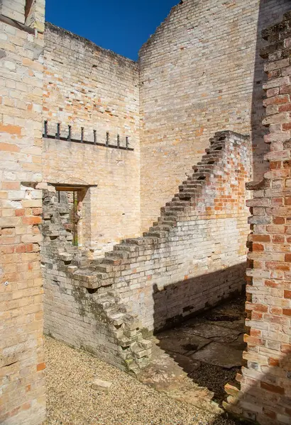 Tarihi Port Arthur Tazmanya harabelerinin içinde güneş ışığıyla aydınlanan tuğla duvarlar, parmaklıklı pencereler, sömürge mimarisi, parlak mavi gökyüzünün altında, Avustralyalı sömürge mirası sergileniyor.