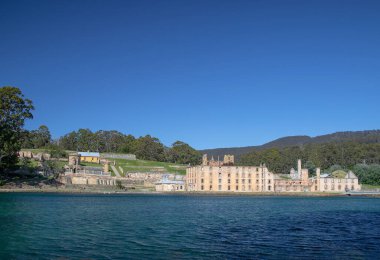 Historic ruins at Port Arthur, Tasmania, Australia surrounded by lush greenery and calm waters under a clear blue sky. High quality photo clipart