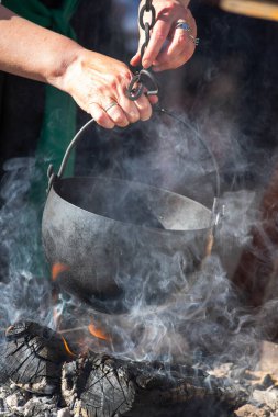 Geleneksel dökme demir tencere ve su ısıtıcısı açık ateş çukurunda asılı ve tarihi kampta yükselen dumanla birlikte.. 