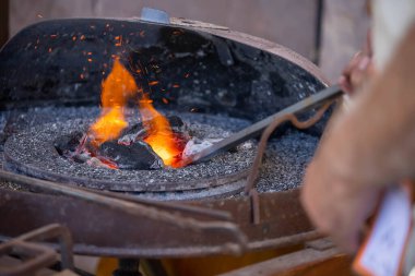 Geleneksel kalpazanlık gösterisi sırasında demircilerin elleri çekiçle örse metal çubuk tutarken yakın plan.