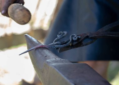 Geleneksel kalpazanlık gösterisi sırasında demircilerin elleri çekiçle örse metal çubuk tutarken yakın plan.