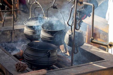 Geleneksel dökme demir tencere ve su ısıtıcısı açık ateş çukurunda asılı ve tarihi kampta yükselen dumanla birlikte.