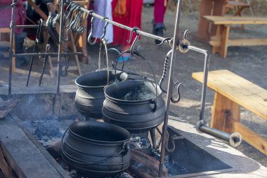 Geleneksel dökme demir tencere ve su ısıtıcısı açık ateş çukurunda asılı ve tarihi kampta yükselen dumanla birlikte.