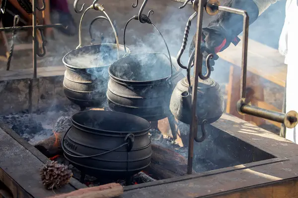 Geleneksel dökme demir tencere ve su ısıtıcısı açık ateş çukurunda asılı ve tarihi kampta yükselen dumanla birlikte.