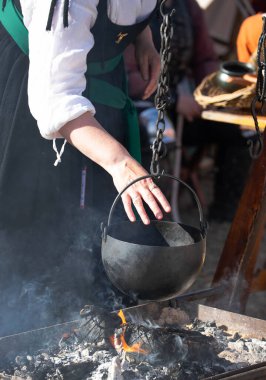 Geleneksel dökme demir tencere ve su ısıtıcısı açık ateş çukurunda asılı ve tarihi kampta yükselen dumanla birlikte. Yüksek kalite fotoğraf