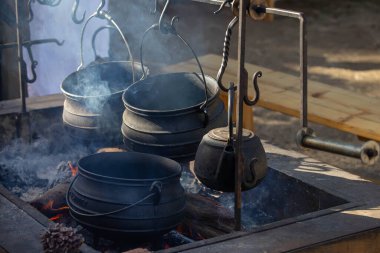 Geleneksel dökme demir tencere ve su ısıtıcısı açık ateş çukurunda asılı ve tarihi kampta yükselen dumanla birlikte. Yüksek kalite fotoğraf