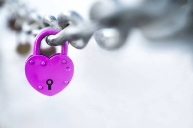 Pink heart shaped lock hangs from bridge chain, wedding custom is symbol of eternal love, copy space