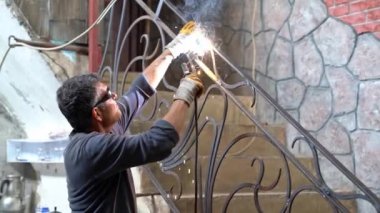 Koruyucu gözlük takan adam kaynak makinesiyle metal kaynak yapıyor, kaynak makinesinden kıvılcımlar çıkıyor.