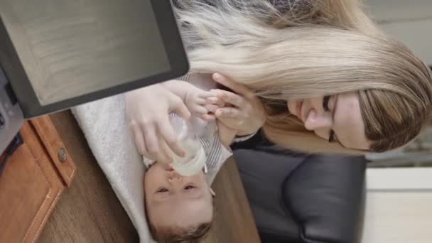 女商人在办公室的桌面上用瓶子喂孩子 孩子出生后工作的概念 垂直录像 — 图库视频影像