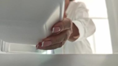 Kadın buzdolabını açıyor ve tek kullanımlık plastik yiyecek kabını çıkarıyor. İçeriden bakıyor..