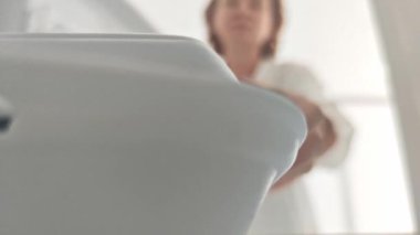 Kadın buzdolabını açar ve tek kullanımlık plastik yiyecek kabını çıkarır. Buzdolabının içini görür..