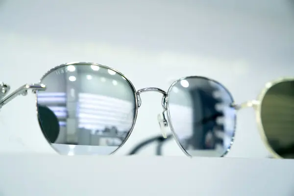 Yansıtıcı gümüş lensli yuvarlak güneş gözlüklerinin yakın çekimi, şık modern tasarım ve metalik çerçeveler, moda ileri aksesuarları, minimalist ekran, perakende atmosferi