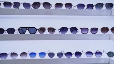 Beyaz raflarda canlı mercek renkleri sergilenen şık güneş gözlükleri, perakende alanında organize seçimler, moda aksesuarlarının sergilenmesi ve alışveriş ortamının geliştirilmesi.