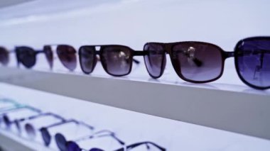 Beyaz raflarda düzenlenmiş güneş gözlükleri, canlı mercek renkleri ve şık tasarımlar, organize moda aksesuarları seçimi, alışverişçiler için perakende ortamı geliştirme.