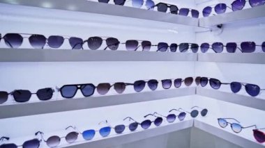 Beyaz raflara dizilmiş şık güneş gözlükleriyle çok renkli lens renkleri, düzenli moda aksesuarları seçimi, müşterileri canlı ve renkli perakende sunumuna davet ediyor.