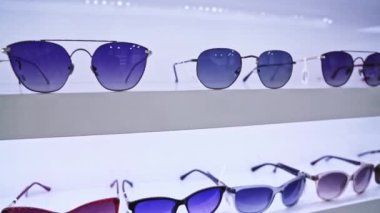 Sergilenen çeşitli renklerdeki güneş gözlükleri, modern göz giyiminin yakın çekimi, organize raf sunumu, moda aksesuarları ve perakende mağazası atmosferinin vurgulanması .