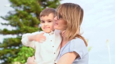 Anne ve genç oğul arasındaki duygusal kucaklaşma, güçlü aile bağı ve bağın altını çizmek, açık havada sarılmak, doğal güzellik, sevgi ve sıcaklığın ifadesi.