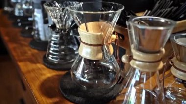 Ahşap tezgahta kahve demleme seti, el yapımı kahve aletleri, cam kahve makineleri Chemex, barista esaslarına yakın çekim, sıcak kırsal atmosfer, modern kahve kültürü, davet edici kafeterya iç mekanları..