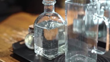 Sıcak ışıkta boş bardağın yanında duran cam şişe, minimalist içecek seti berraklığı ve saflığı sembolize ediyor, temiz tasarım ve şeffaf dokulara odaklanıyor.