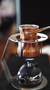 Gaz ocağında bakır kahve demliği, geleneği sembolize ediyor ve Türk kahvesinin özünü çağrıştırıyor. El yapımı demleme işlemi yavaş ve dikkatli kahve yapma sanatını yakalar.