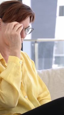 Sarı Gömlekli Yetişkin Kadın, Akıllı Telefon Oturuyor ve Gözlük Giydiriyor, Dijital Göz Süzümü Konsepti ve Rahat Kapalı Çevrede Modern Yaşam Tarzı.